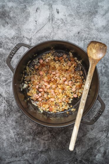 Zwiebeln und Speck in einem Topf karamellisieren